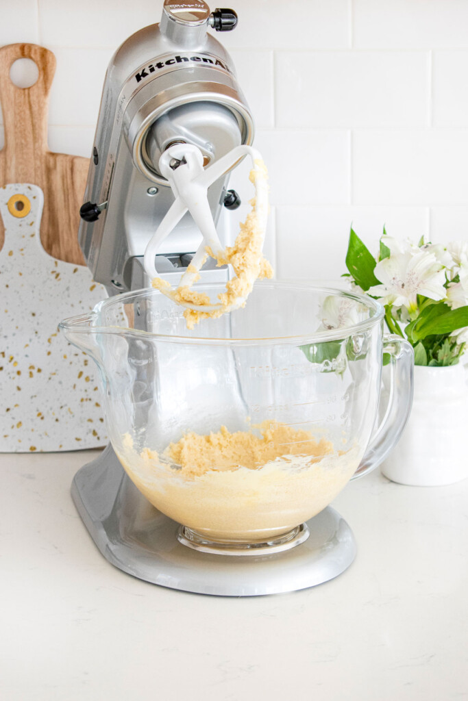 creamed butter and sugar in a glass stand mixing bowl on a white marble counter with fresh flowers.