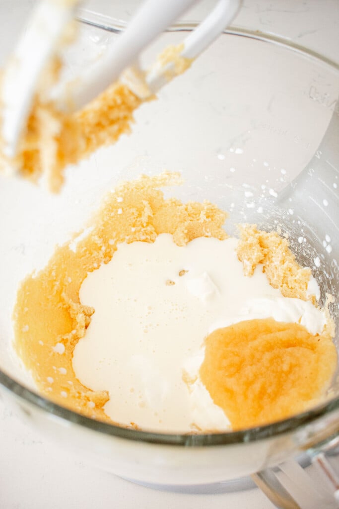 wet ingredients being added to creamed butter and sugar in a glass stand mixing bowl.