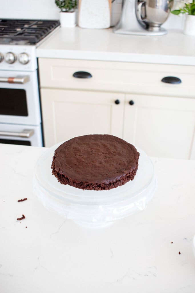 a cake stand with one layer of chocolate cake on it on a white marble counter.