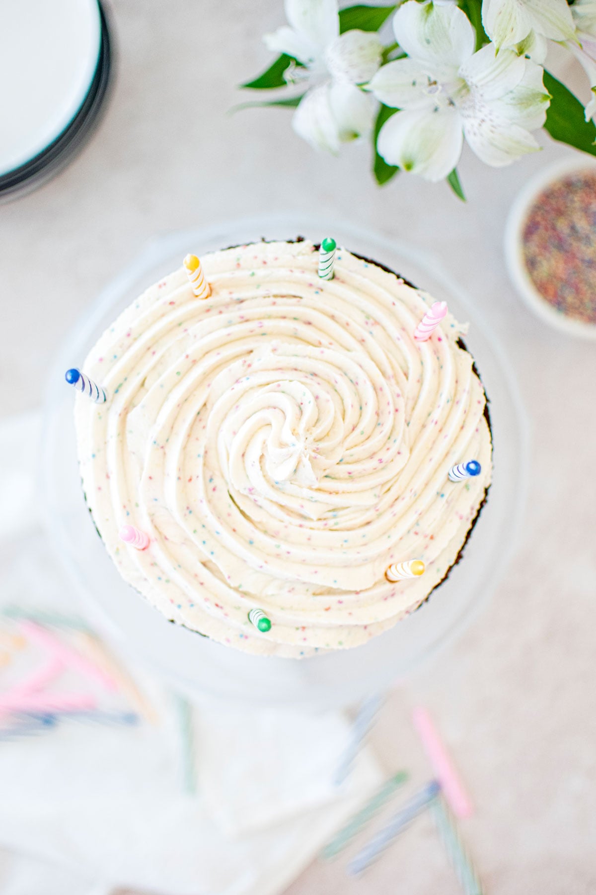 eggless birthday cake with cream cheese frosting swirl and birthday candles on top on a table with fresh flowers.