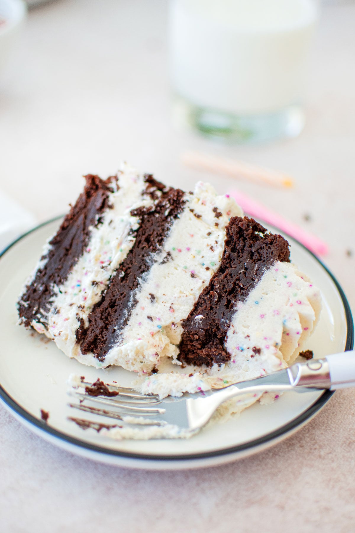 eggless birthday cake with cream cheese frosting slice on a cake plate with a fork and glass of milk.
