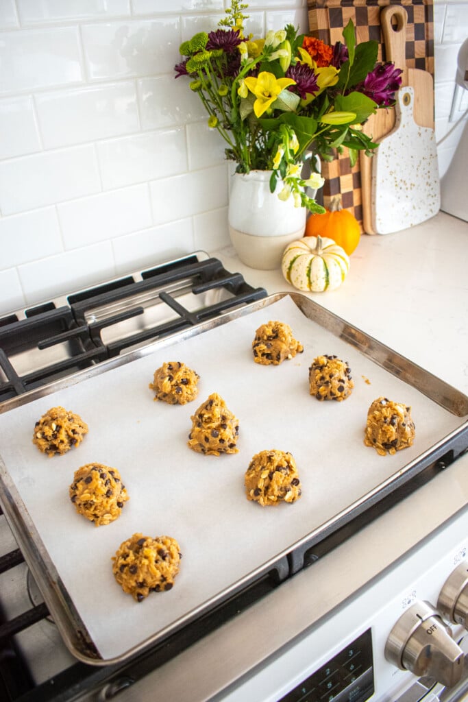 baking sheet with oatmeal cashew butter chocolate chip cookie dough balls spread out evenly sitting on top of an oven.