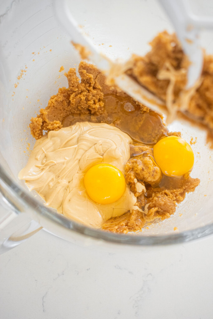 creamed light brown sugar and butter with cashew butter and eggs in a glass mixing bowl on a marble counter.
