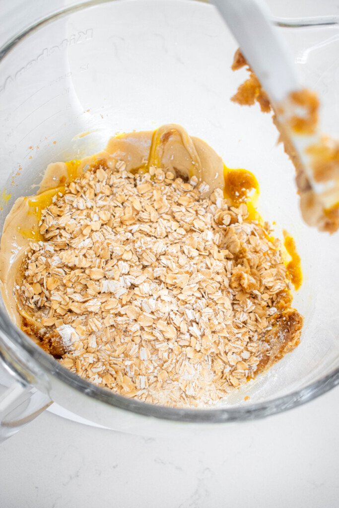 ingredients for oatmeal cashew butter chocolate chip cookies in a glass mixing bowl on a marble counter.