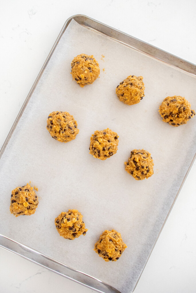 oatmeal cashew butter chocolate chip cookie dough balls on a baking sheet on a marble counter.
