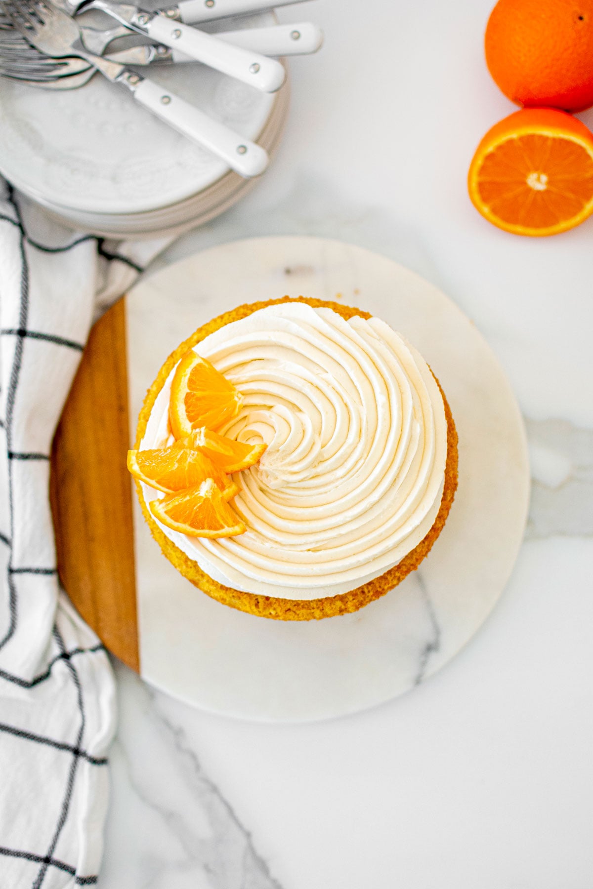 orange ginger carrot cake frosted naked style with fresh orange slices on a marble serving board.