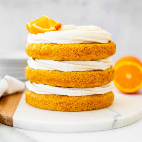 orange ginger carrot cake frosted naked style with fresh orange slices on a marble serving board.