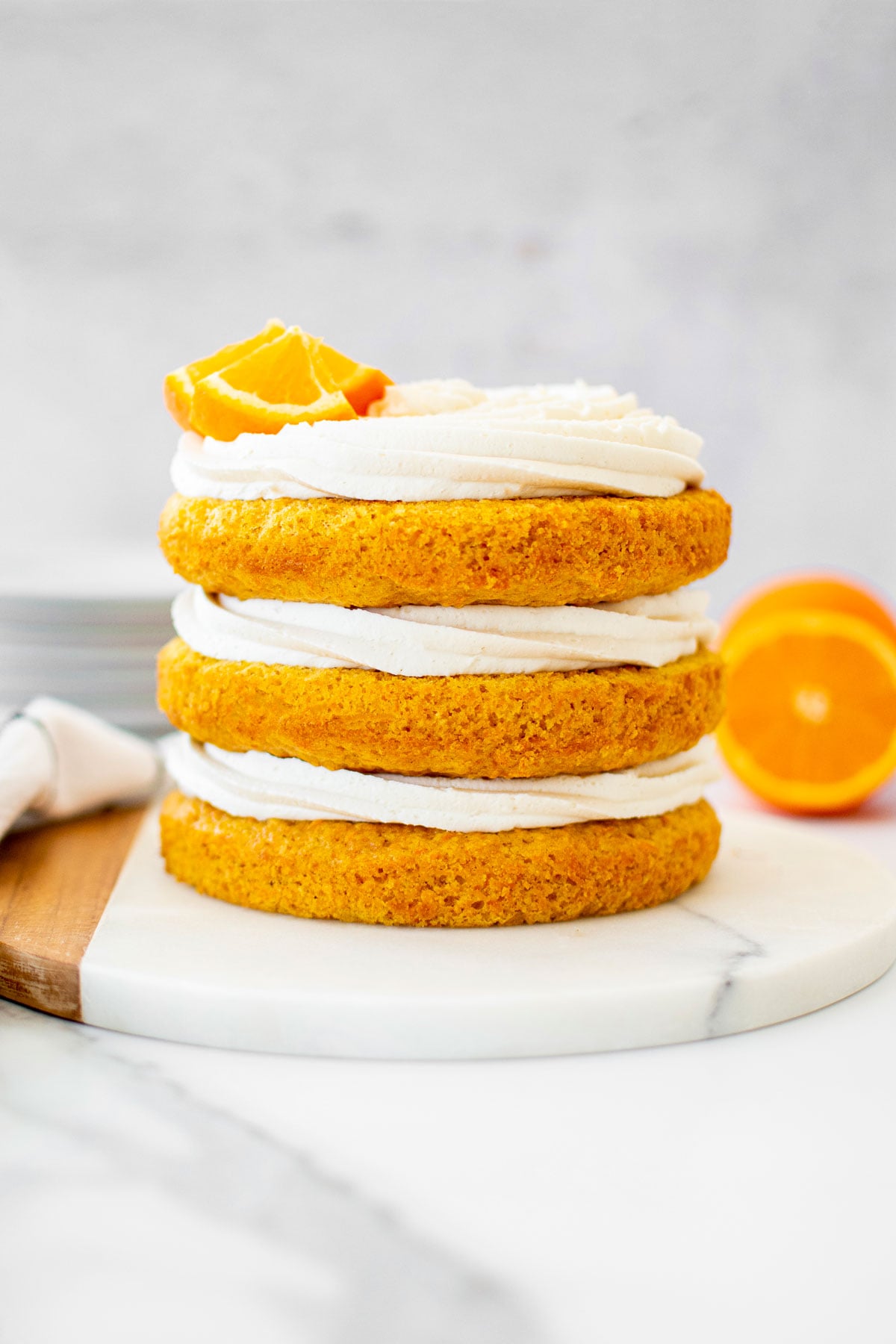 orange ginger carrot cake frosted naked style with fresh orange slices on a marble serving board.