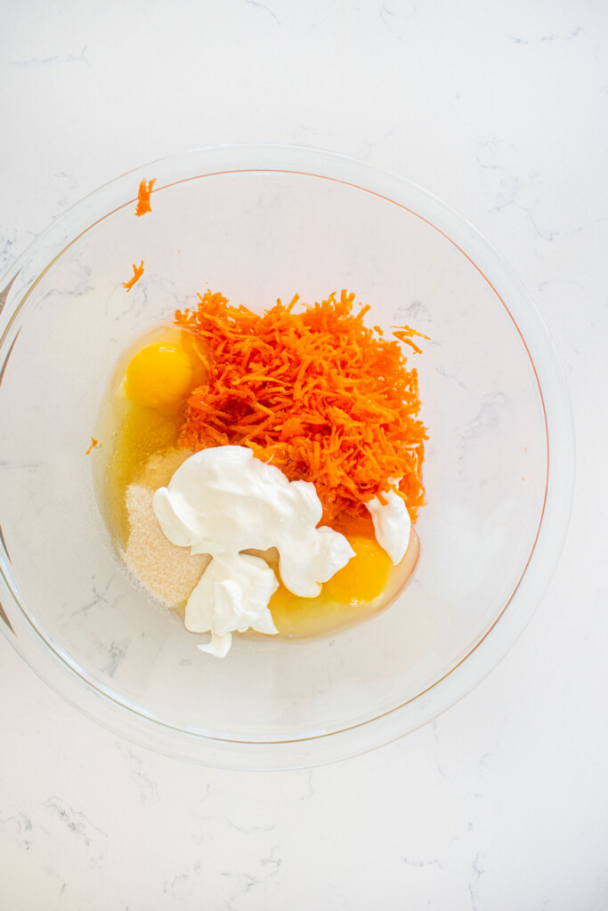 wet ingredients for orange ginger carrot cake in a glass mixing bowl on a white marble counter.
