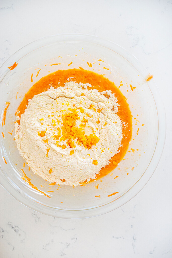 wet ingredients for orange ginger carrot cake in a glass mixing bowl with a whisk on a white marble counter.