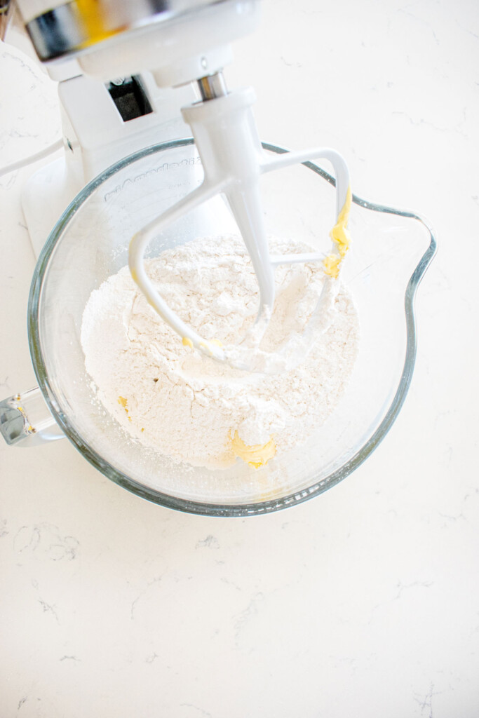 ingredients for orange cream cheese frosting in a glass mixing bowl on a white marble counter.