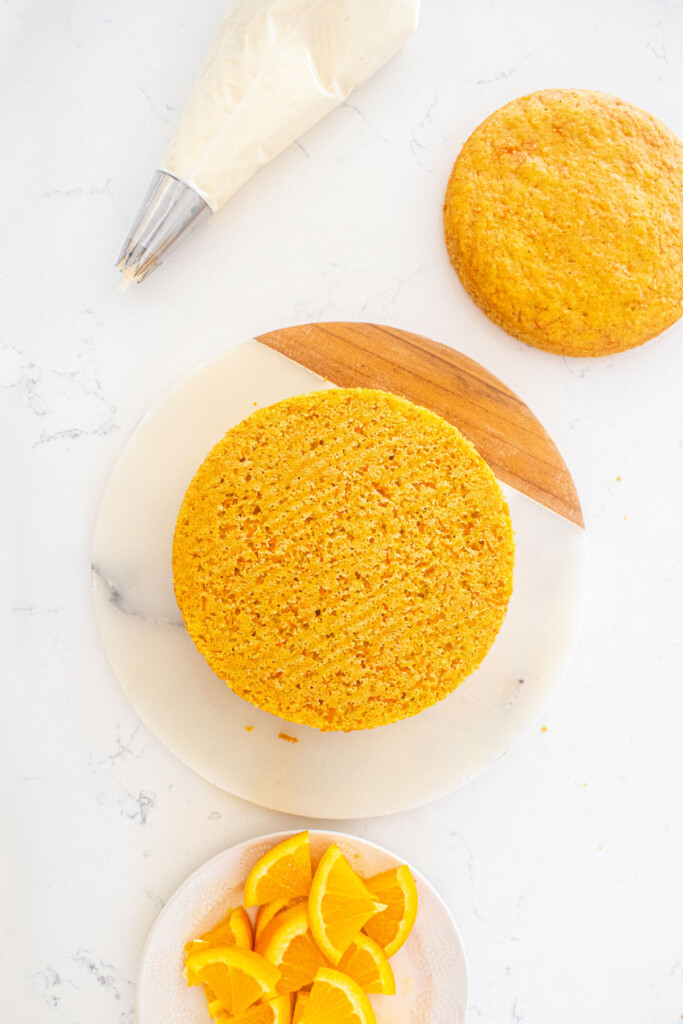 orange ginger carrot cake being assembled on a marble serving board on a white marble counter.