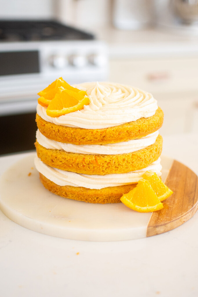 orange ginger carrot cake frosted naked style with fresh orange slices on a marble serving board.