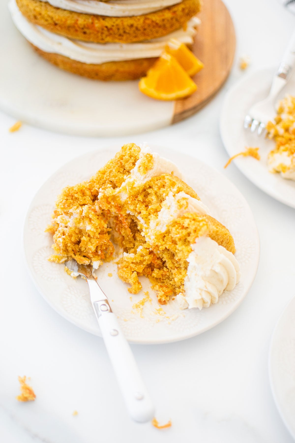 slice of orange ginger carrot cake on a plate with a fork on a marble table.