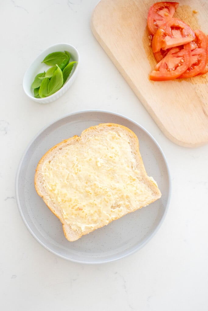sourdough bread on a gray plate with garlic butter spread on top on a white countertop with sliced tomatoes on the side.
