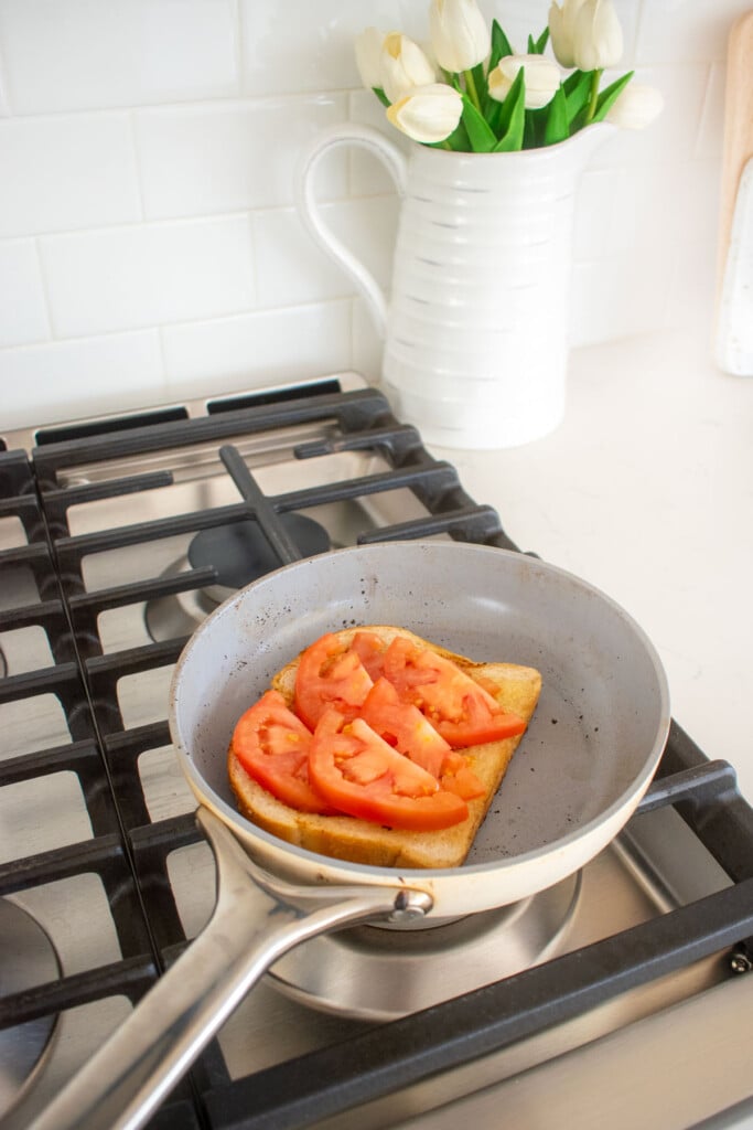 sourdough bread being toasted in a skillet with tomatoes on top.