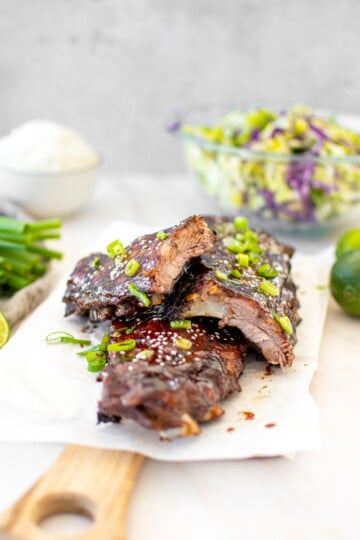 sticky sweet chili baby back ribs with green onions on a serving board on a marble countertop.