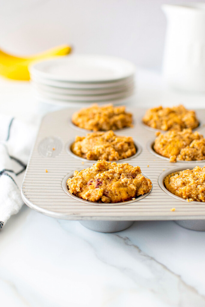 muffin pan of eggless banana raspberry muffins on a white marble counter.
