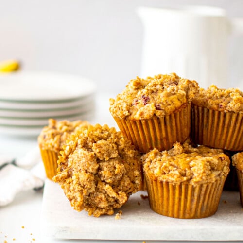 eggless banana raspberry muffins on a white marble counter with a pitcher of milk.