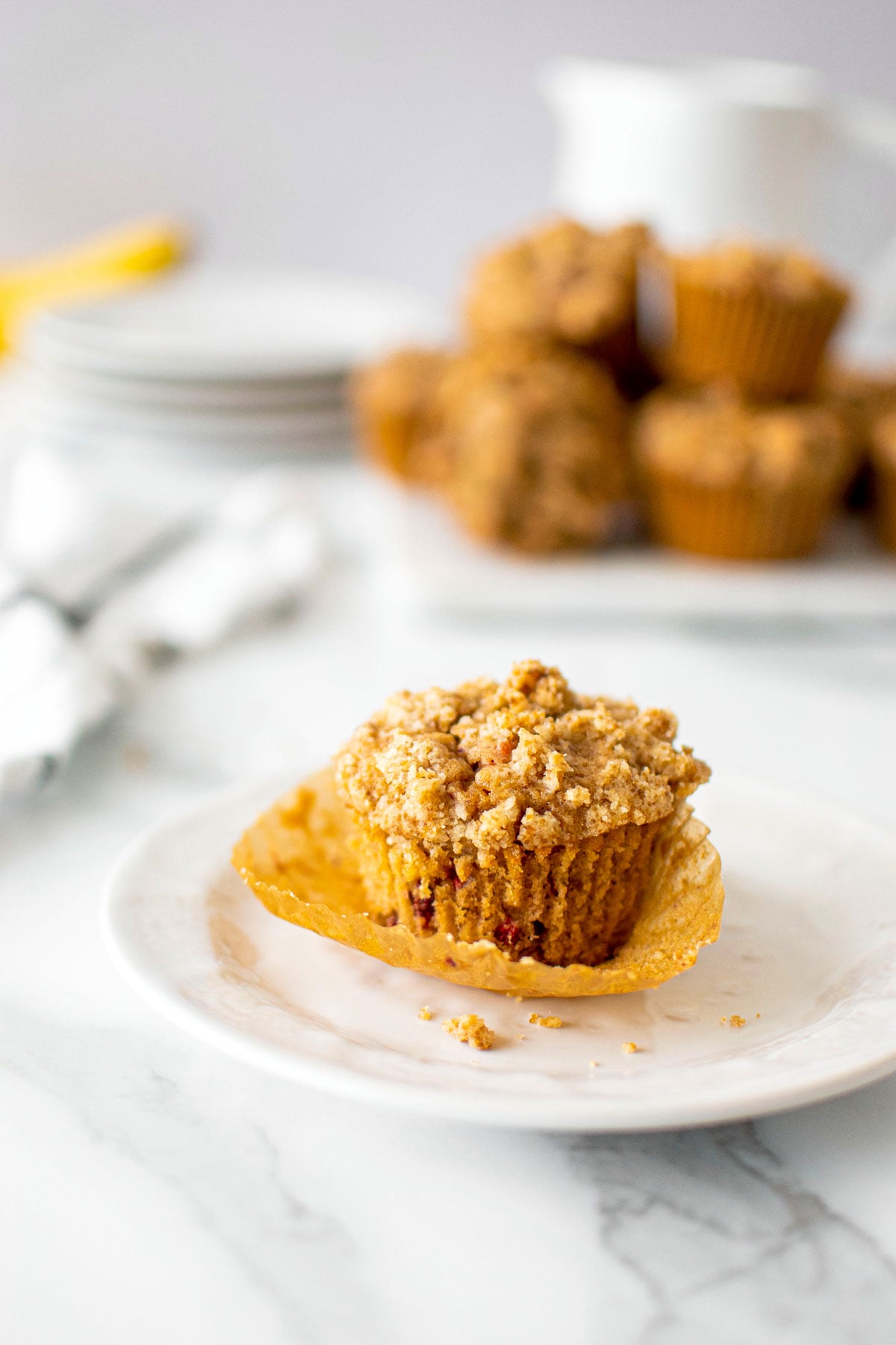 eggless banana raspberry muffin on a white plate with muffin liner being pulled off.