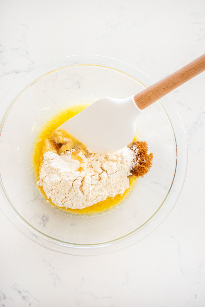 ingredients for crumble topping in a glass bowl with a spatula on a marble counter.