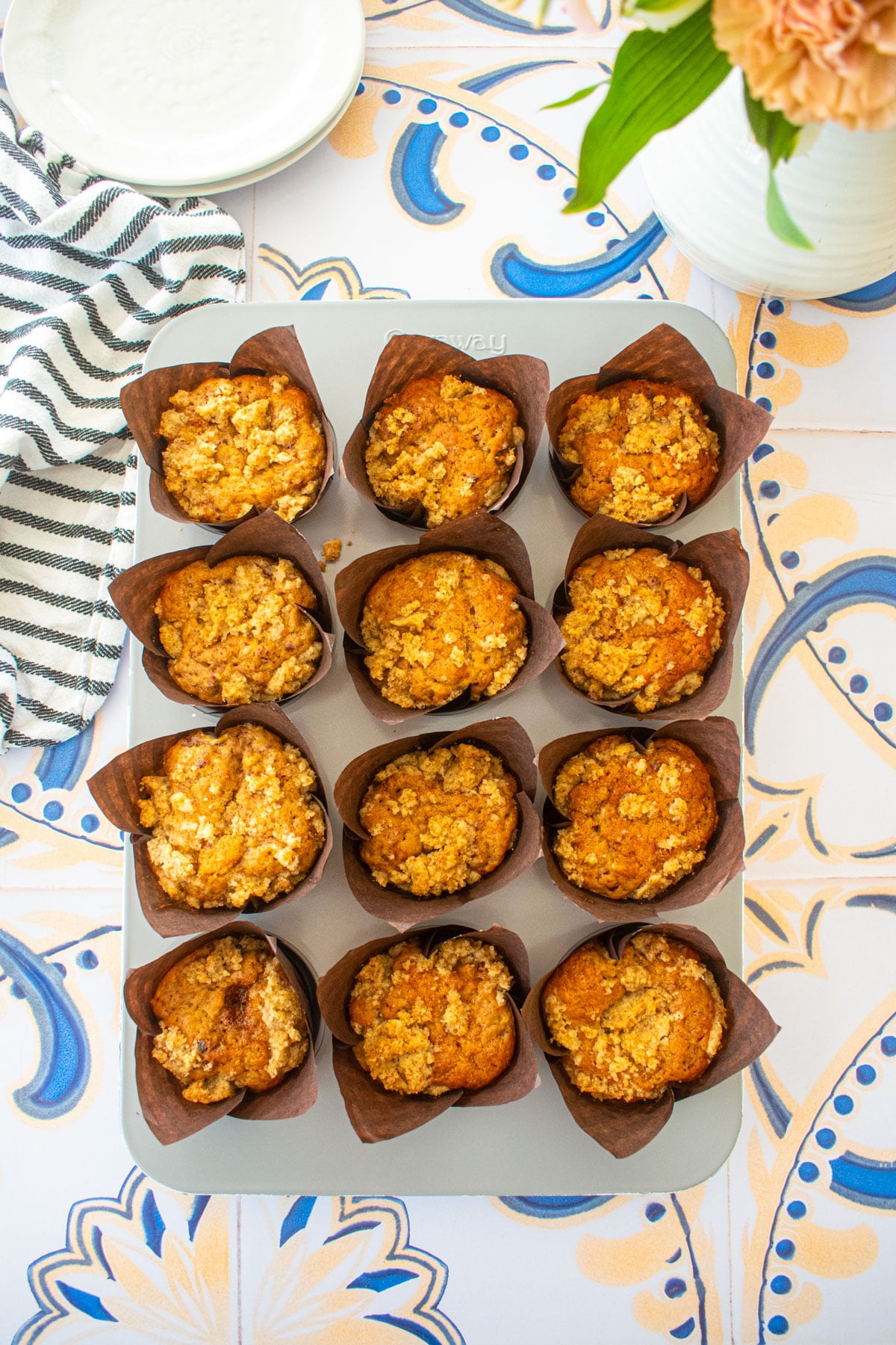 muffin pan with eggless banana raspberry muffins on a tile table with small plates and fresh flowers.