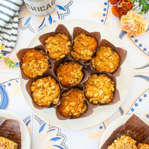 round plate of eggless banana raspberry muffins on a tile table with a mug of coffee and flowers.