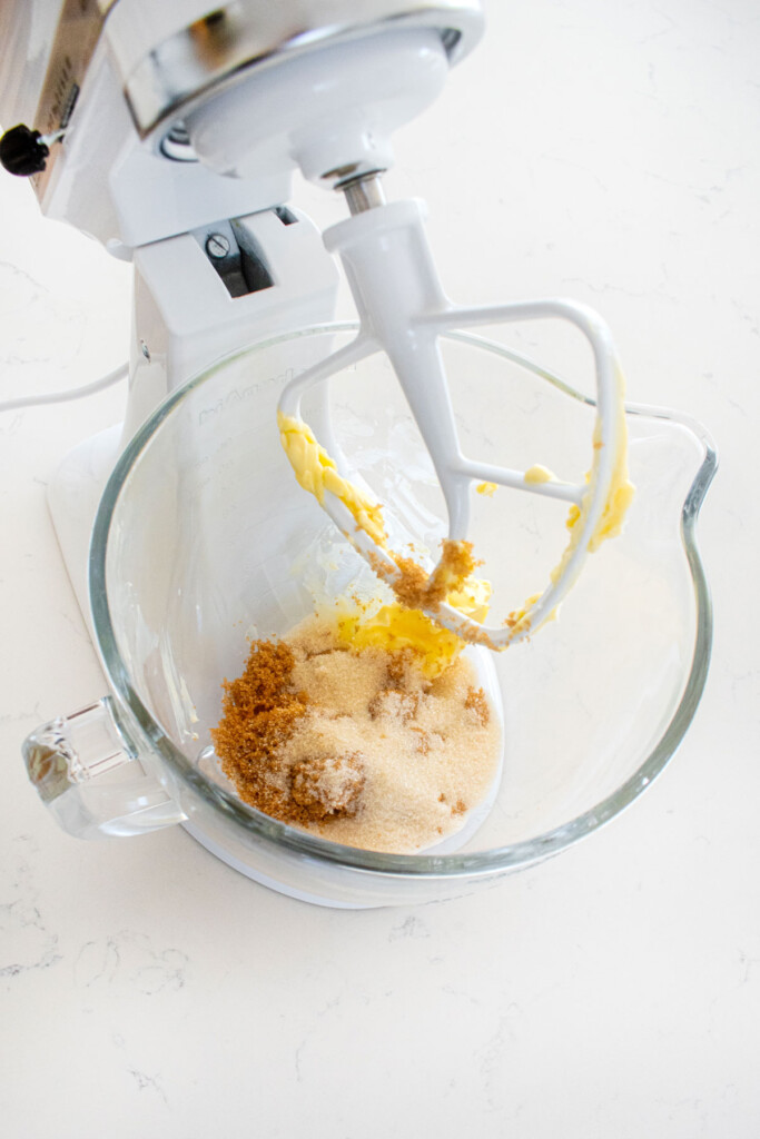 butter and sugar in a glass mixing bowl on a white marble counter.
