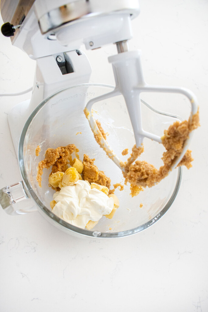 ingredients for eggless banana raspberry muffin batter in a glass mixing bowl on a white marble counter.