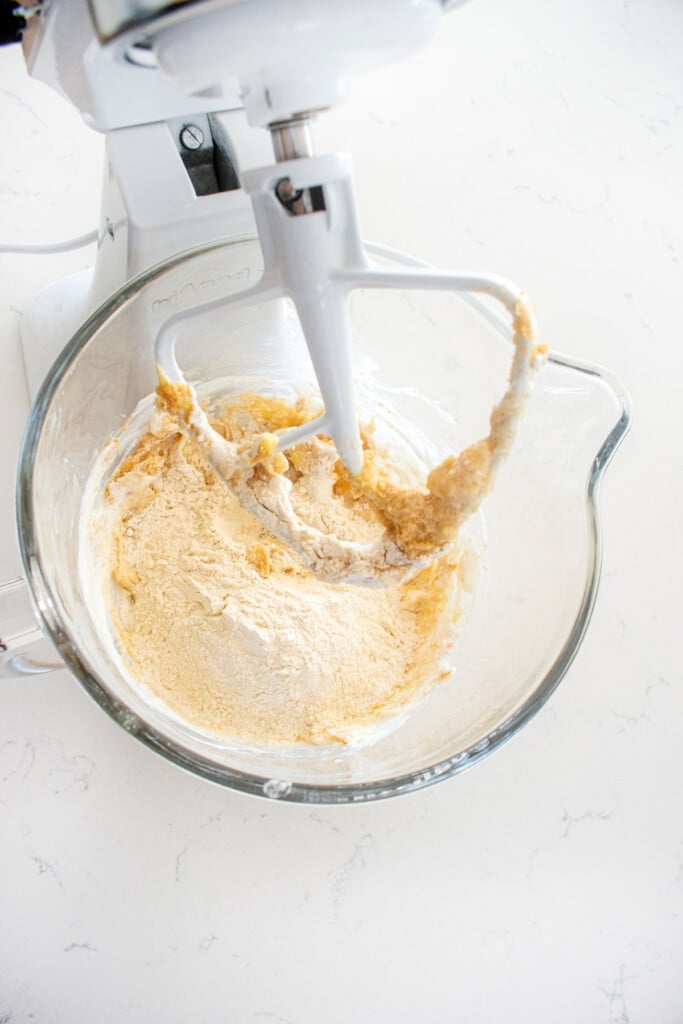 ingredients for eggless banana raspberry muffin batter in a glass mixing bowl on a white marble counter.