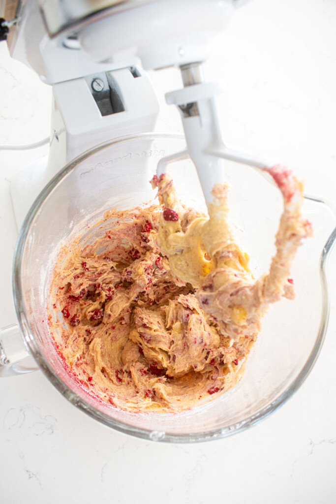 eggless banana raspberry muffin batter in a glass mixing bowl on a white marble counter.