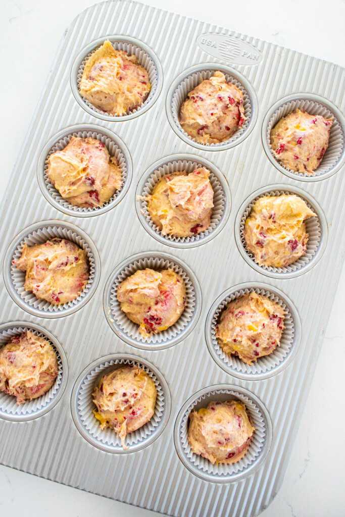 eggless banana raspberry muffins in a muffin pan on a white marble counter.