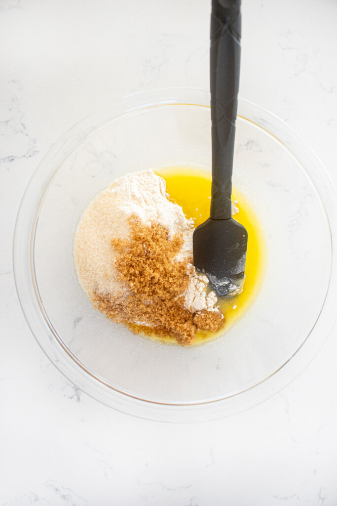 ingredients for streusel topping mixed with a spatula in a glass mixing bowl on a white marble counter.