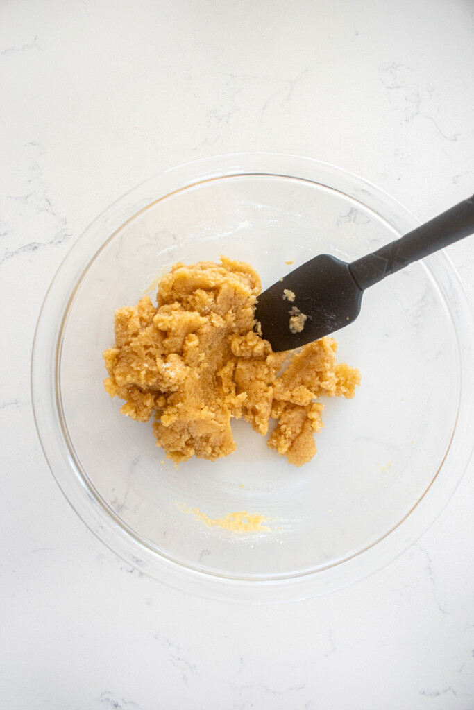 streusel topping mixed with a spatula in a glass mixing bowl on a white marble counter.