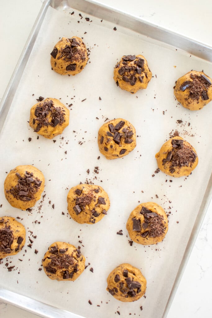 eggless sea salt dark chocolate chunk cookie dough balls on a baking sheet on a marble counter.