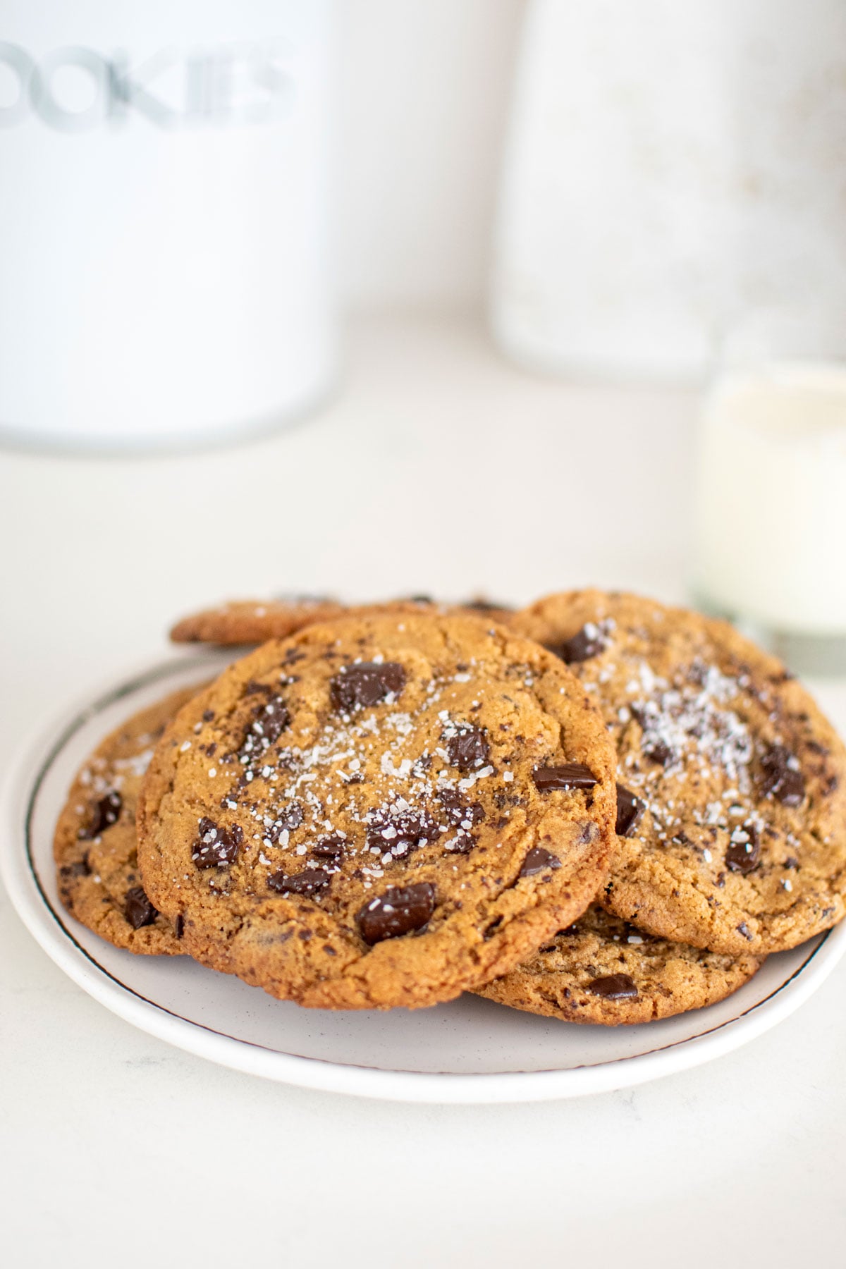 plate of eggless sea salt dark chocolate chunk cookies with flaky sea salt and glass of milk on a marble counter.