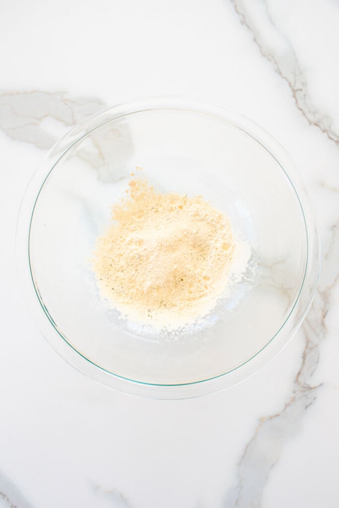 garlic powder, ranch seasoning and white cheddar powder in a glass bowl on a white marble counter.