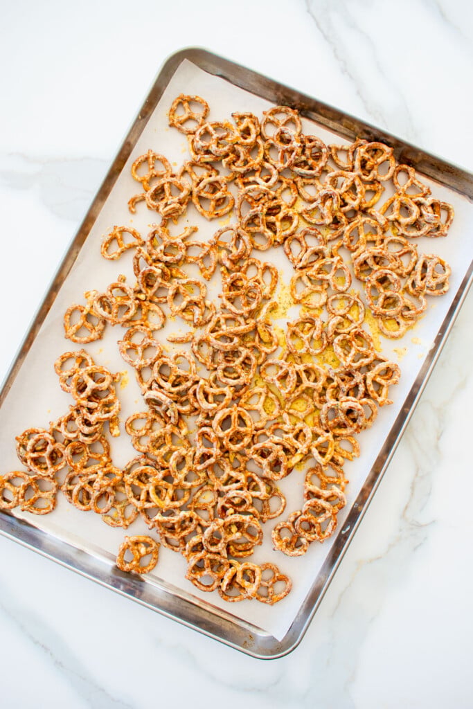 garlic ranch pretzels with white cheddar spread out onto a baking sheet with parchment paper on a white marble counter.