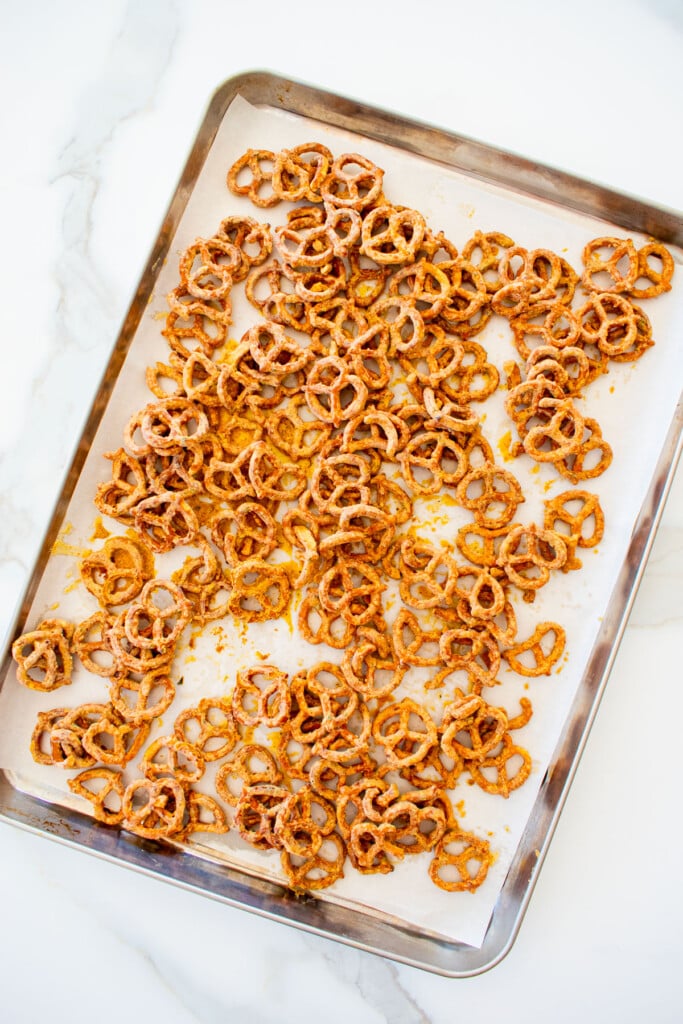 garlic ranch pretzels with white cheddar spread out onto a baking sheet with parchment paper on a white marble counter.