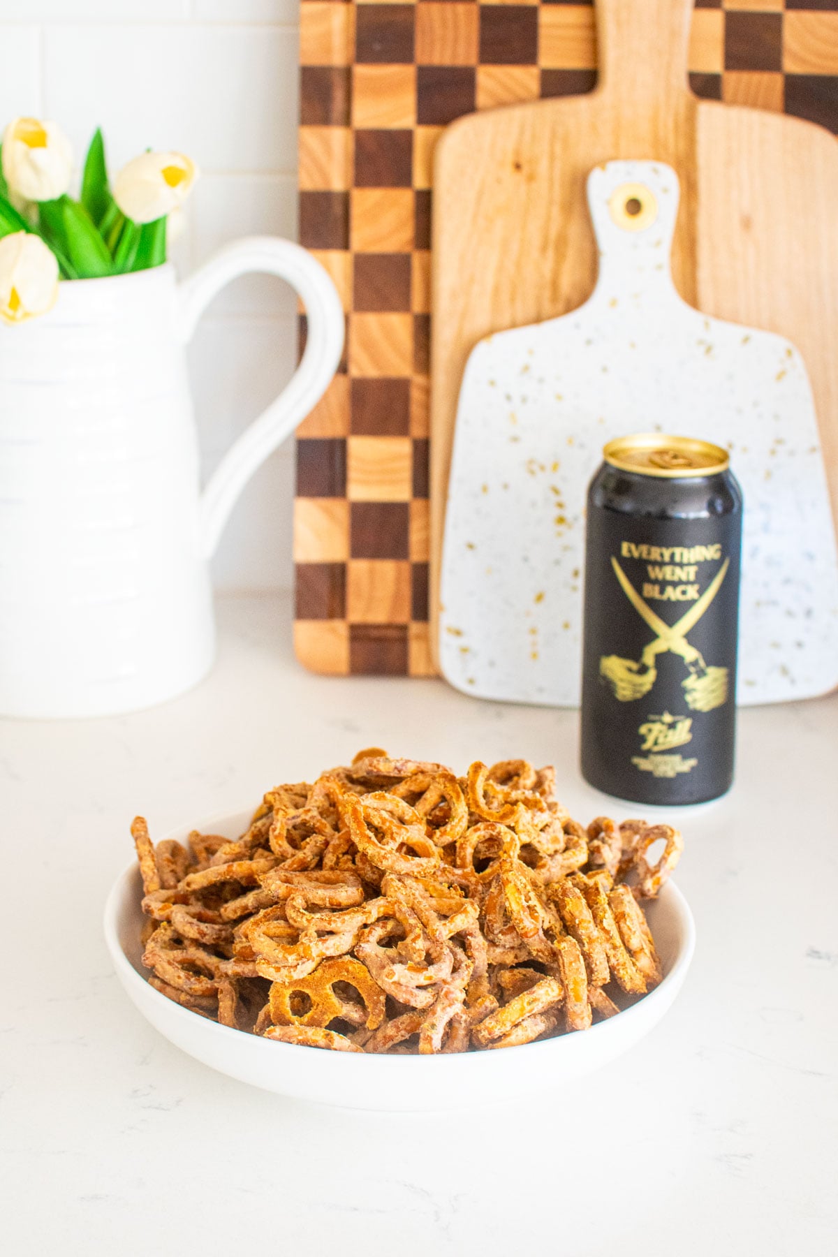 bowl of garlic ranch pretzels with white cheddar on a white marble counter with a beer.