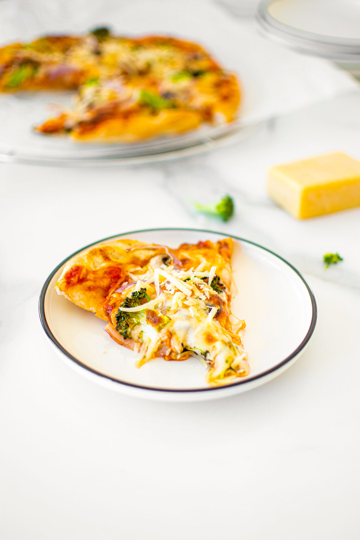 mushroom broccoli pizza slice on a white plate on a white marble countertop.