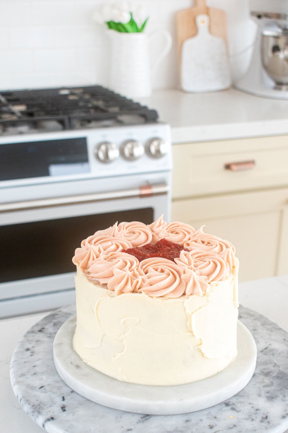 strawberry almond cake on a marble turntable on a white kitchen counter.