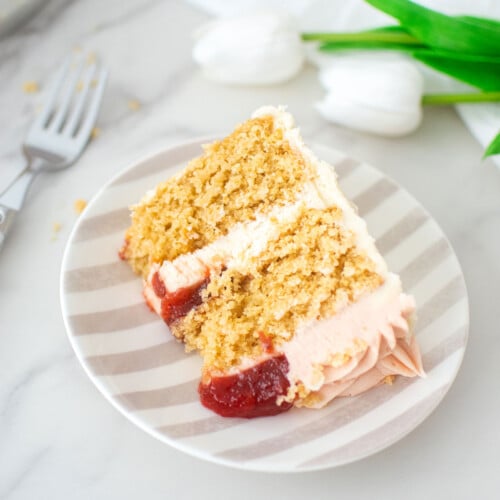 slice of strawberry almond cake on a stripe cake plate on a marble counter.