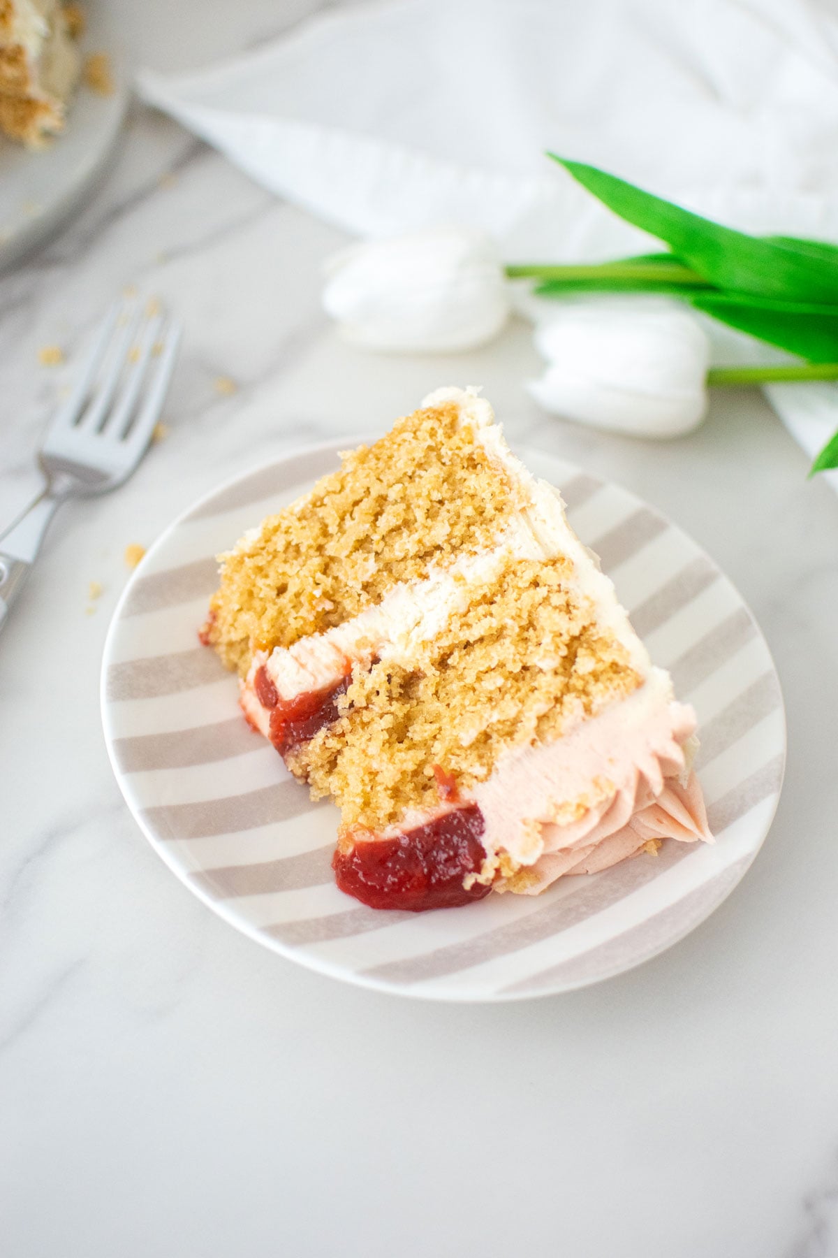 slice of strawberry almond cake on a stripe cake plate on a marble counter.