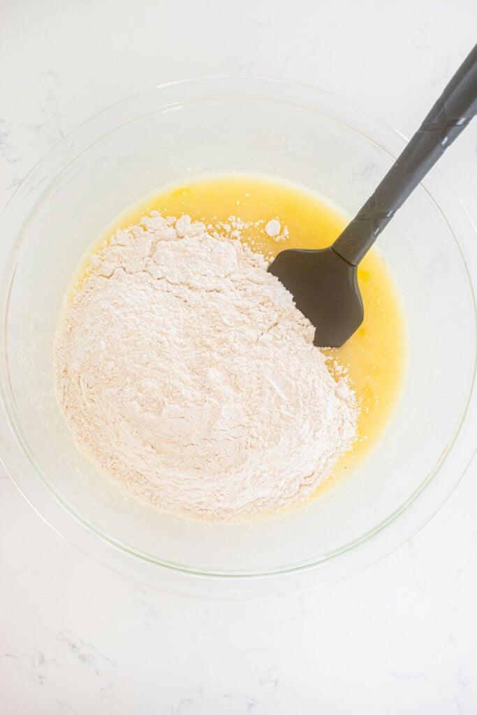 ingredients for almond cake in a glass mixing bowl with a spatula on a white marble counter.