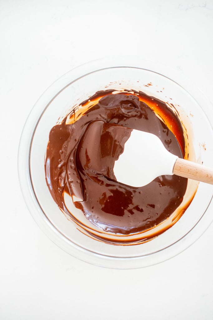 glass bowl of melted chocolate on a white marble counter with a spatula.