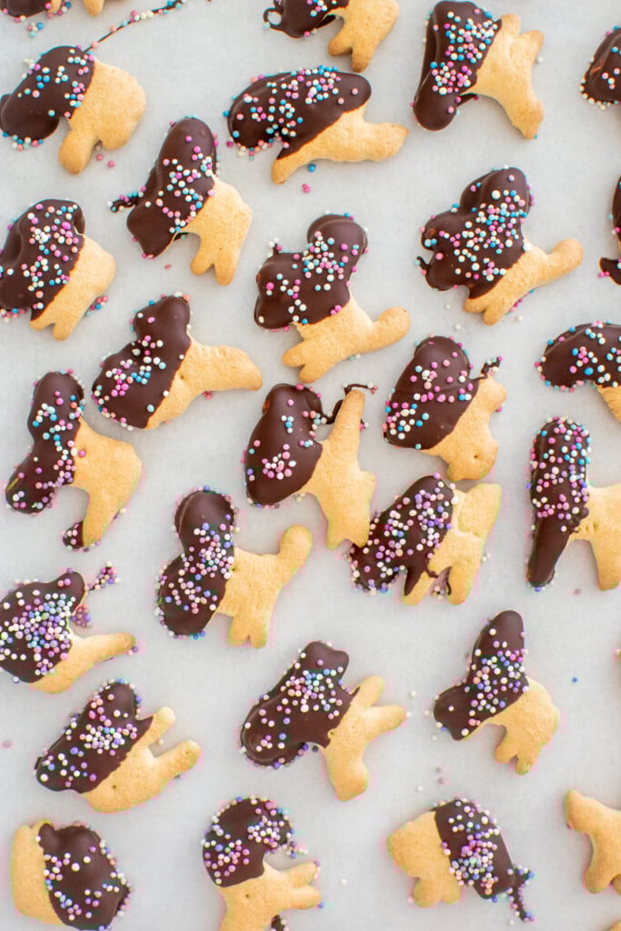 animal crackers half dipped in chocolate with sprinkles on a baking sheet.