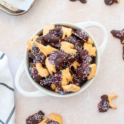 bowl of chocolate dipped animal crackers with sprinkles on a table.