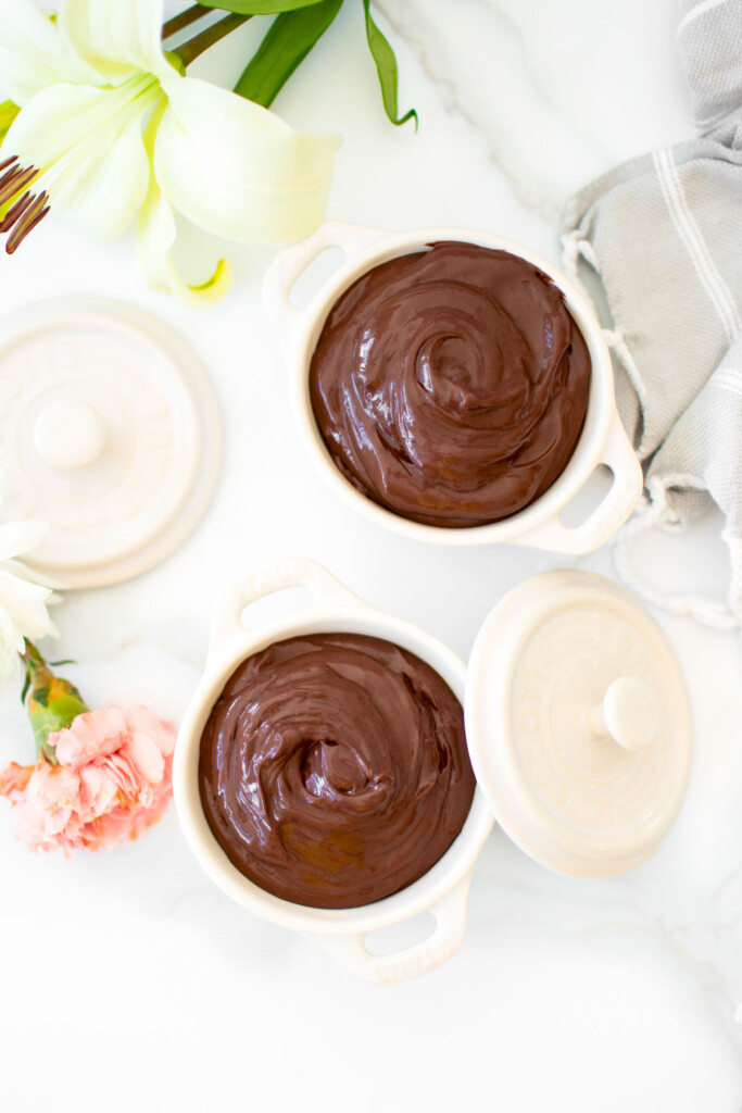 chocolate protein pudding with bone broth in small dutch ovens on a white marble counter with fresh flowers.