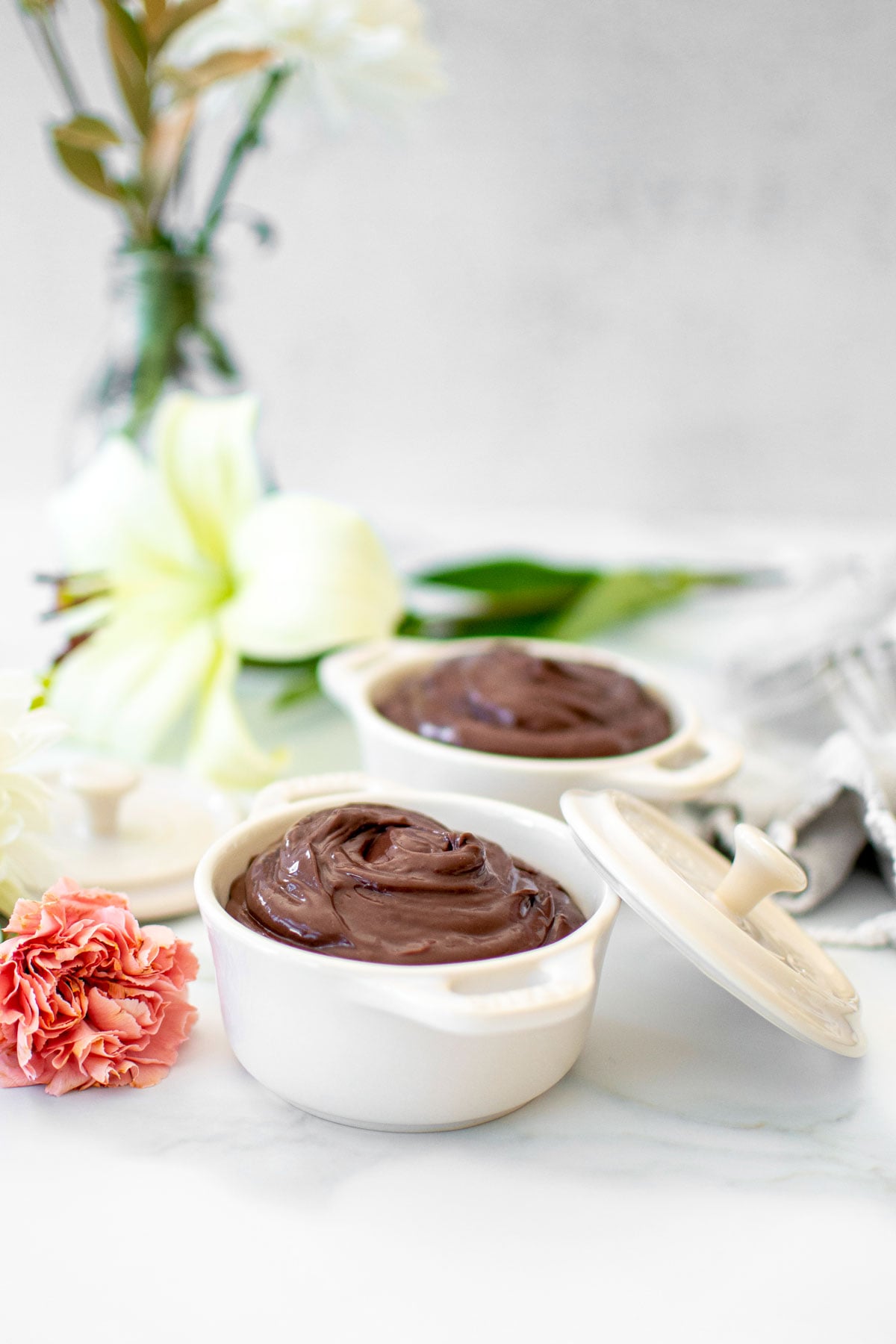 chocolate protein pudding with bone broth in small dutch ovens on a white marble counter with fresh flowers.